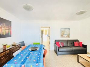 A room with a dining table, chairs, a sofa, and a painting on the wall.