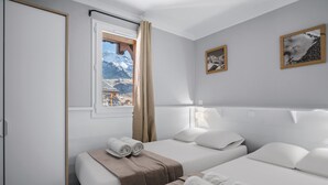 Una camera d'albergo con due letti, una finestra vista montagna e due quadri appesi al muro.