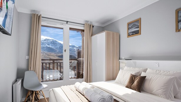 Una camera d'albergo con un letto, una sedia, un armadio e vista sulle montagne attraverso una grande finestra.