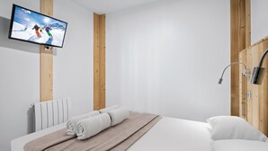 Une chambre d’hôtel moderne équipée d’un lit, d’un téléviseur fixé au mur, d’un mur recouvert de panneaux en bois et d’une douche avec un pommeau de douche à main.