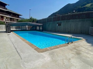 Una piscina rectangular con plataforma de hormigón, una escalera metálica y una montaña al fondo.