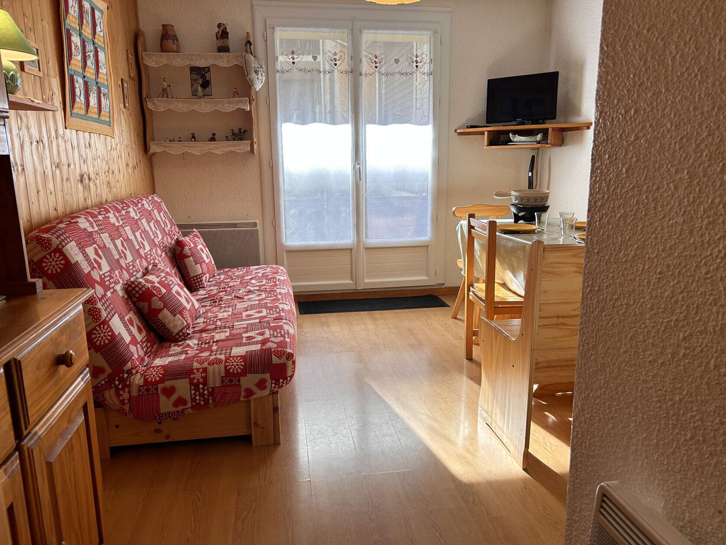 A cozy room with a wooden bed, a small wooden table, a television, and a window with curtains.