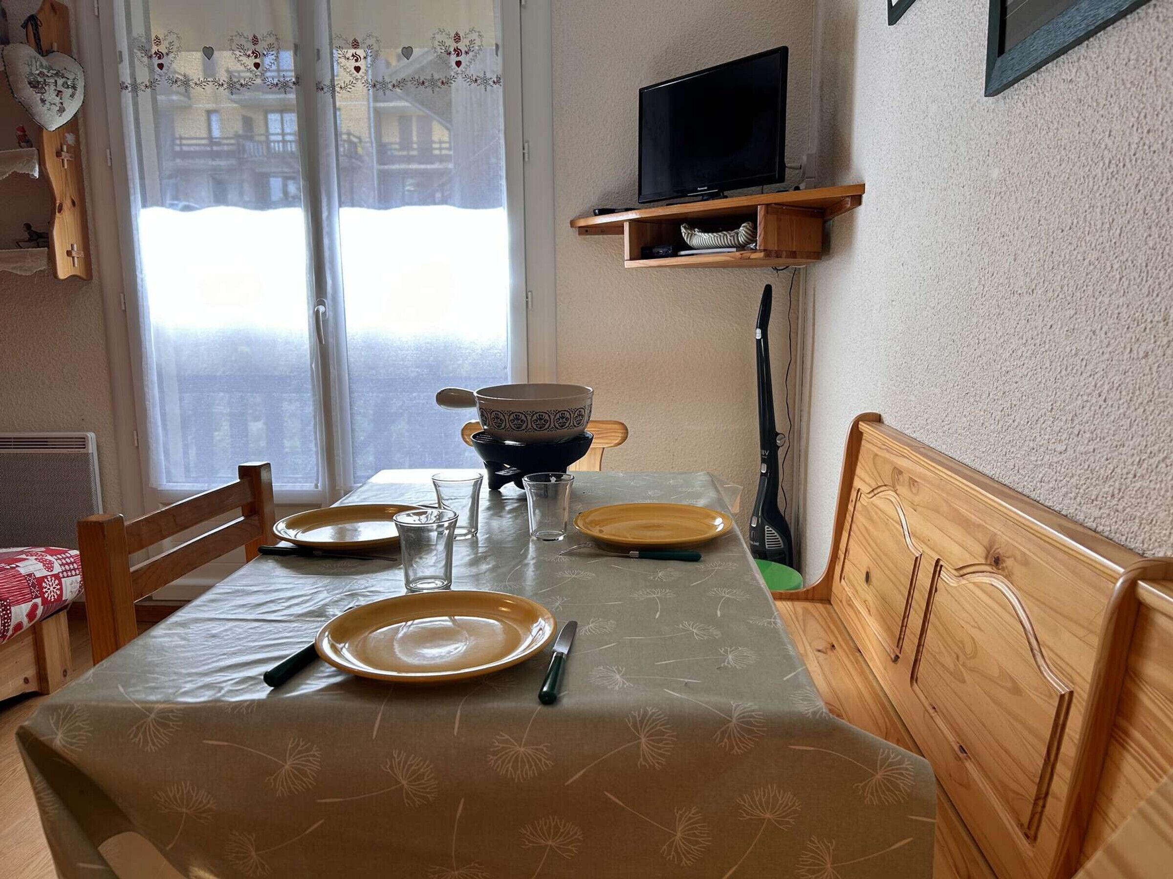 En matplats med ett bord dukat för två personer, en tv ovanför bordet och ett fönster med utsikt över byggnaderna utanför.