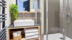 A modern bathroom with a glass shower enclosure, a sink with a mirror above, and a towel rack with folded towels. - 4-star Apartment Les Saisies - SPA, 8 people (Les Saisies)