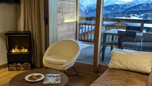 A cozy room with a fireplace, a comfortable armchair, a sofa, and a table with a magazine. - 4-star Apartment Les Saisies - SPA, 8 people (Les Saisies)