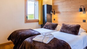 A bedroom with two beds, wooden walls, a window with yellow curtains, and a wall-mounted lamp. - 4-star Apartment Les Saisies - SPA, 8 people (Les Saisies)
