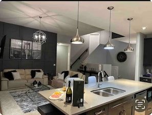 Une cuisine moderne dotée d’un îlot central, de luminaires suspendus et d’un coin repas avec un canapé et une table basse.