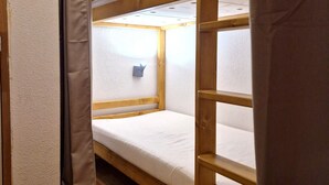 Quarto com beliche, colchão branco e luminária pequena fixada na parede.