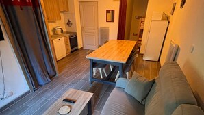 Ett kompakt bostadsutrymme med ett matbord i trä, en soffa och ett köksområde som inkluderar en spis och skåp.