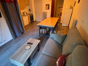 A compact living space with a wooden dining table, a sofa, and a kitchen area including a stove and cabinets.
