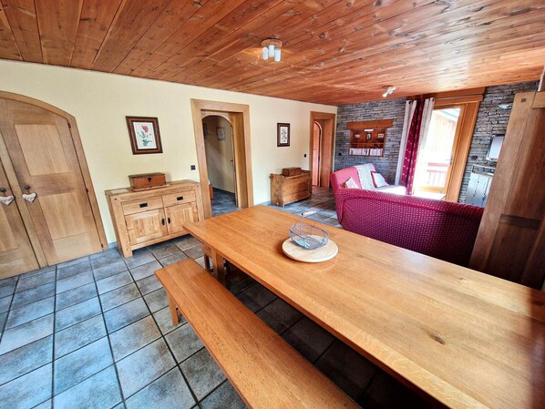A cozy room with a wooden table, benches, a red sofa, and a stone wall.