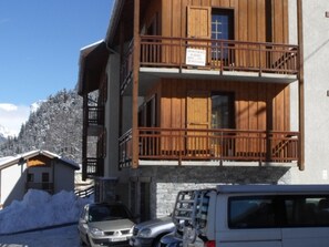 Un edificio de madera con balcón, un coche aparcado y una montaña nevada al fondo.