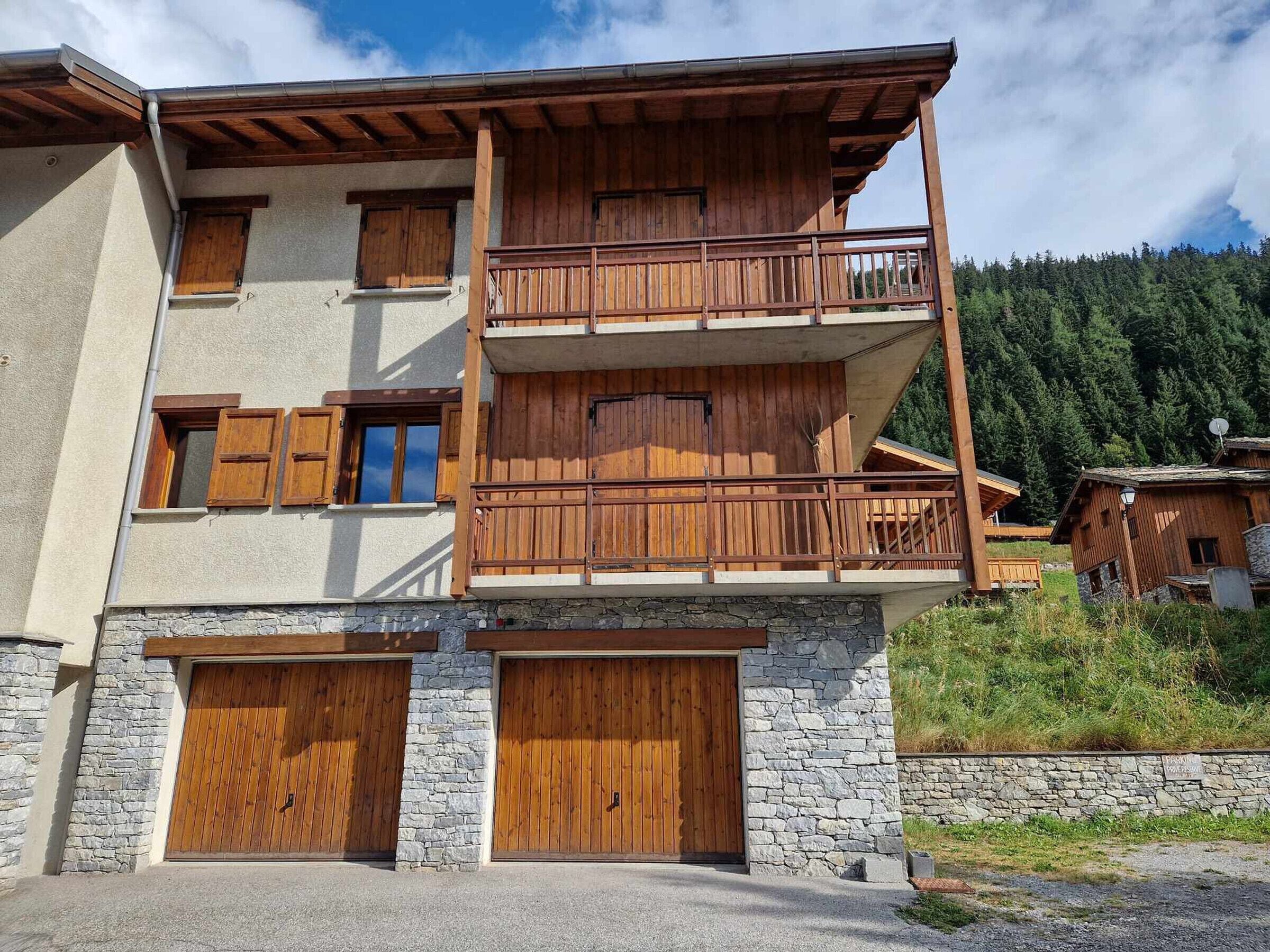 A two-story wooden building with a stone facade, wooden balconies, and a stone wall.