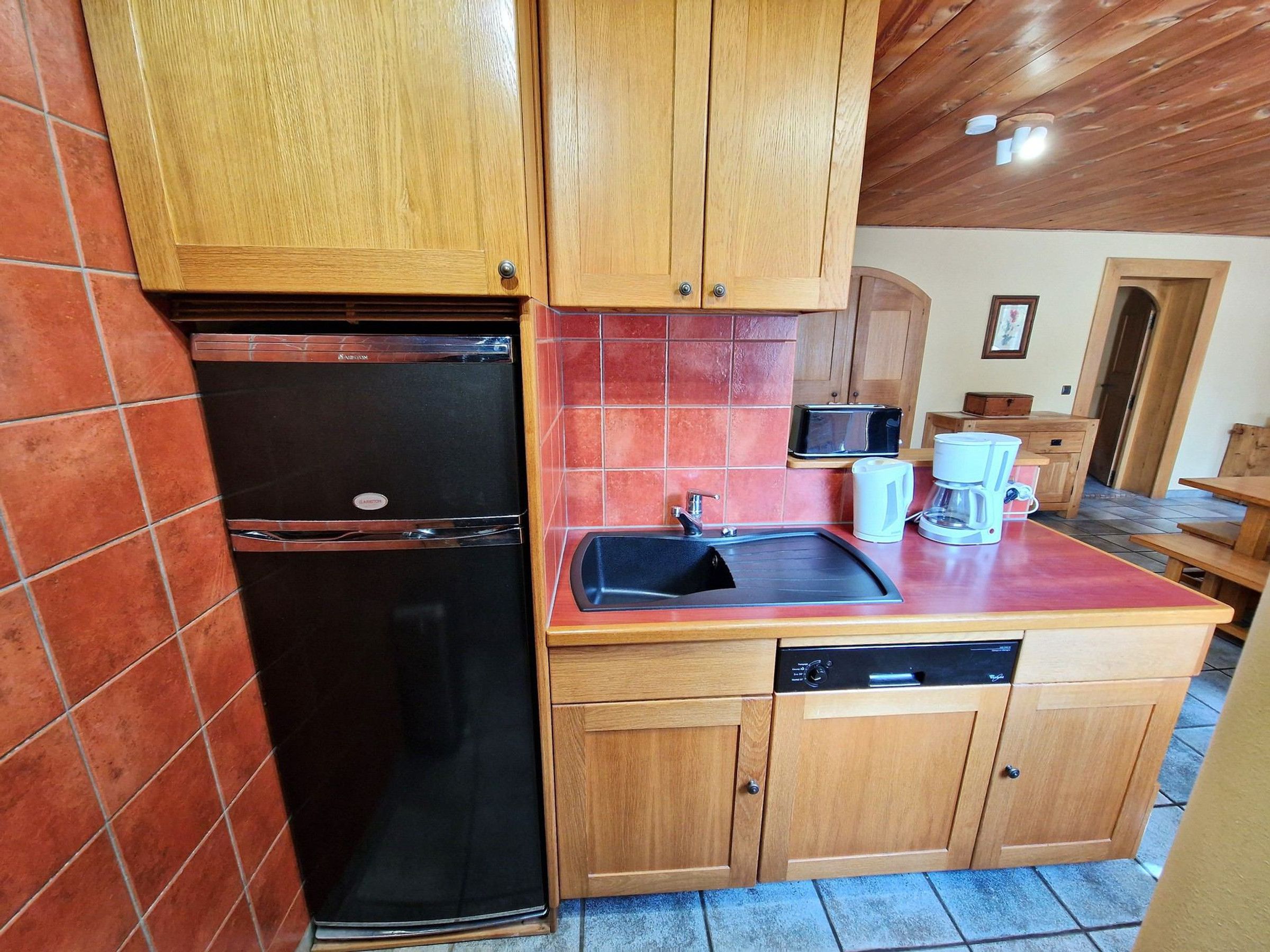 A compact kitchen with wooden cabinets, a black refrigerator, a sink, and a dishwasher.