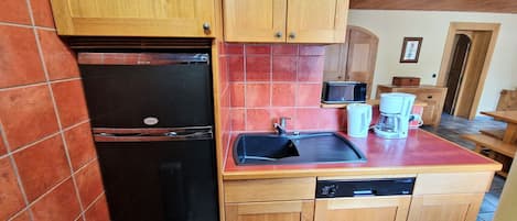 A compact kitchen with wooden cabinets, a black refrigerator, a sink, and a dishwasher.