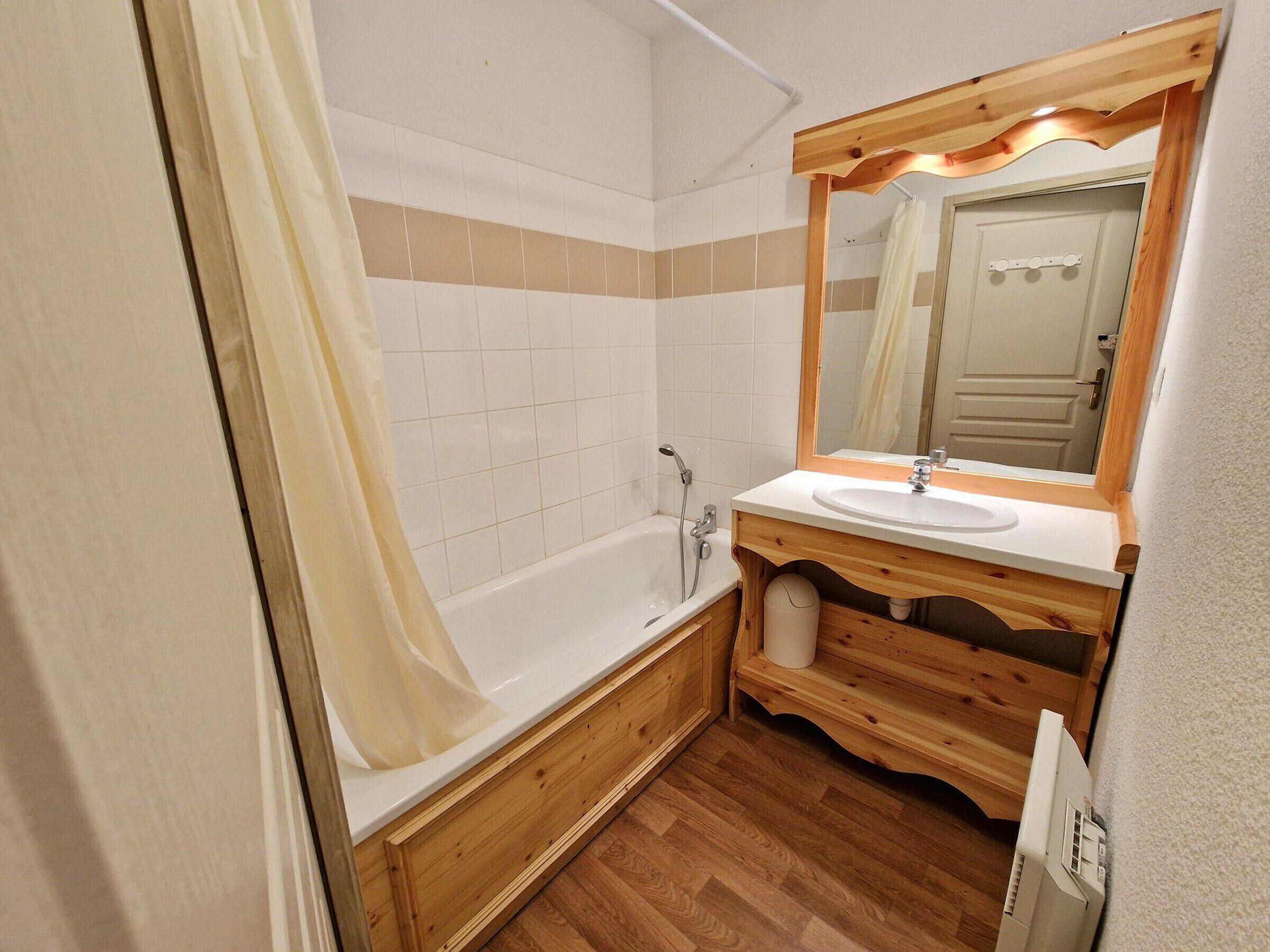 A bathroom with a wooden vanity, a white sink, a mirror, and a bathtub.