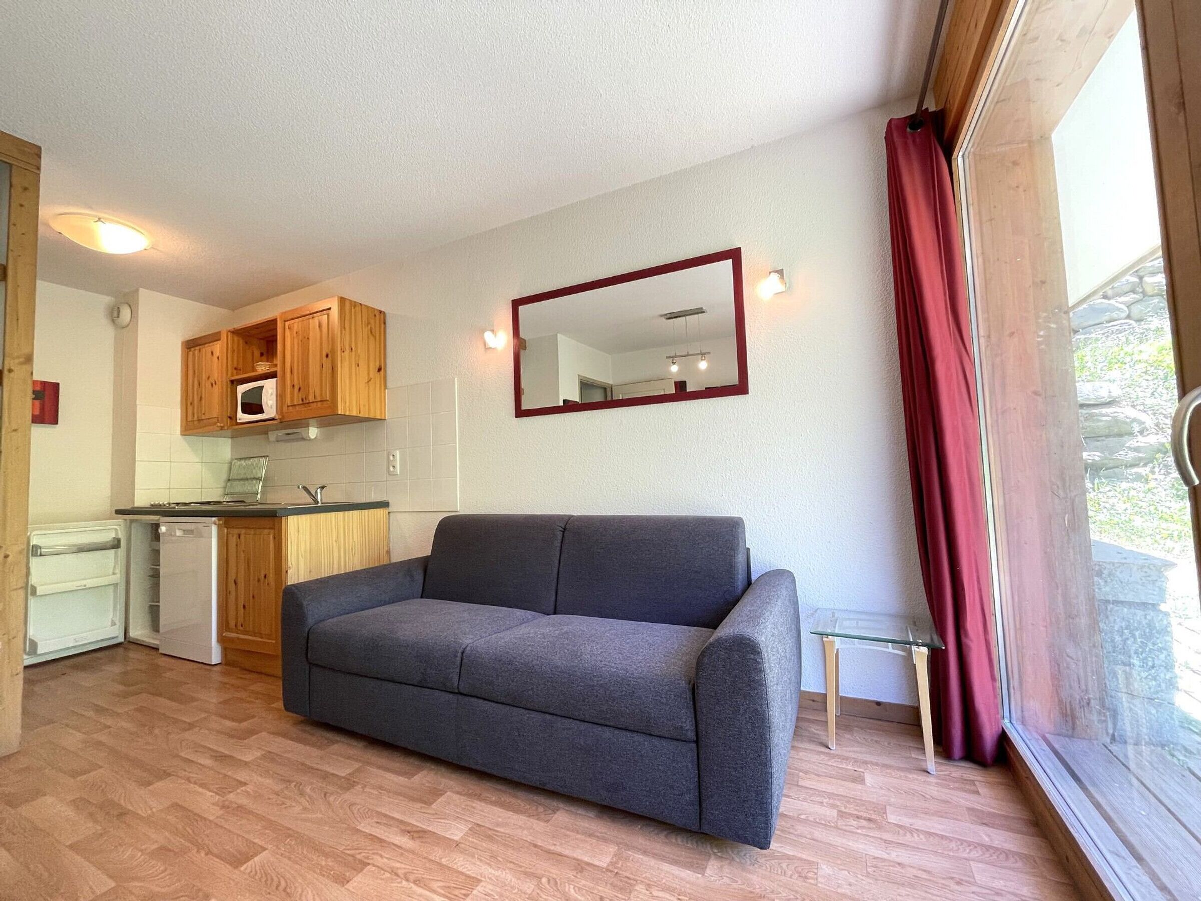 A compact living space with a kitchenette, a sofa, and a large window with curtains.