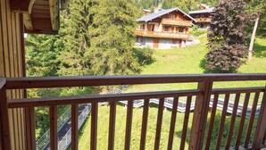 A wooden balcony with a view of a mountain house surrounded by trees. - 3-room apartment, 6 people, at the slopes, pets allowed (Valfréjus)