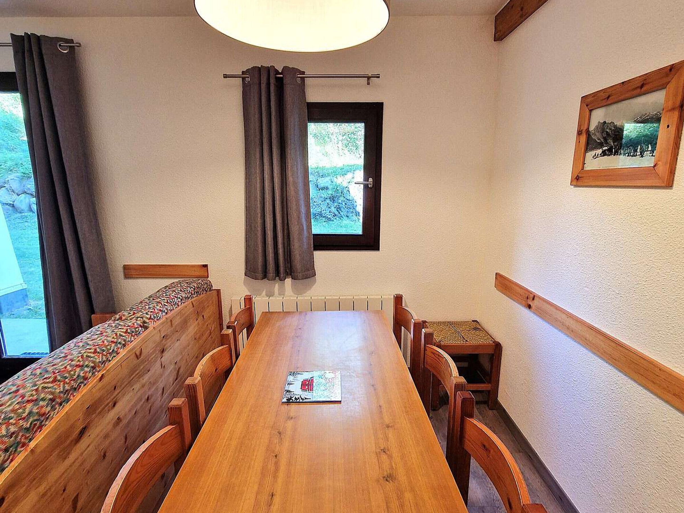 A dining area with a long wooden table, cushioned benches, and a window with curtains.