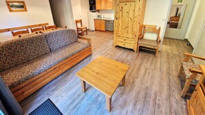 A cozy living room with a sofa, wooden coffee table, and matching chairs. A wooden cabinet and a kitchen area with a microwave and sink are visible. - Large apt 6/8 ppl, direct slopes access, near center, terrace (Valfréjus)