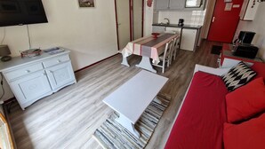 Un espace de vie compact comprenant un coin repas, une kitchenette et un canapé rouge.