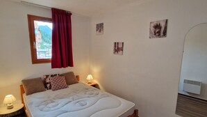 Une chambre à coucher avec un lit, deux tables de chevet, une fenêtre avec des rideaux rouges et un climatiseur fixé au mur.