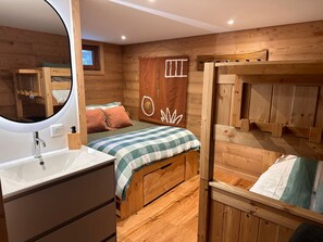 A cozy cabin-style room with a wooden interior, a bunk bed, a small bathroom with a sink, and a mirror.