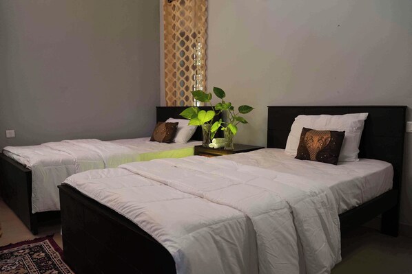 Une chambre d’hôtel avec deux lits simples, une table de chevet ornée d’une plante et un rideau décoratif.