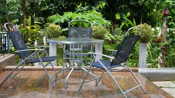 Un patio con una mesa redonda y dos sillas, rodeado de abundante vegetación.