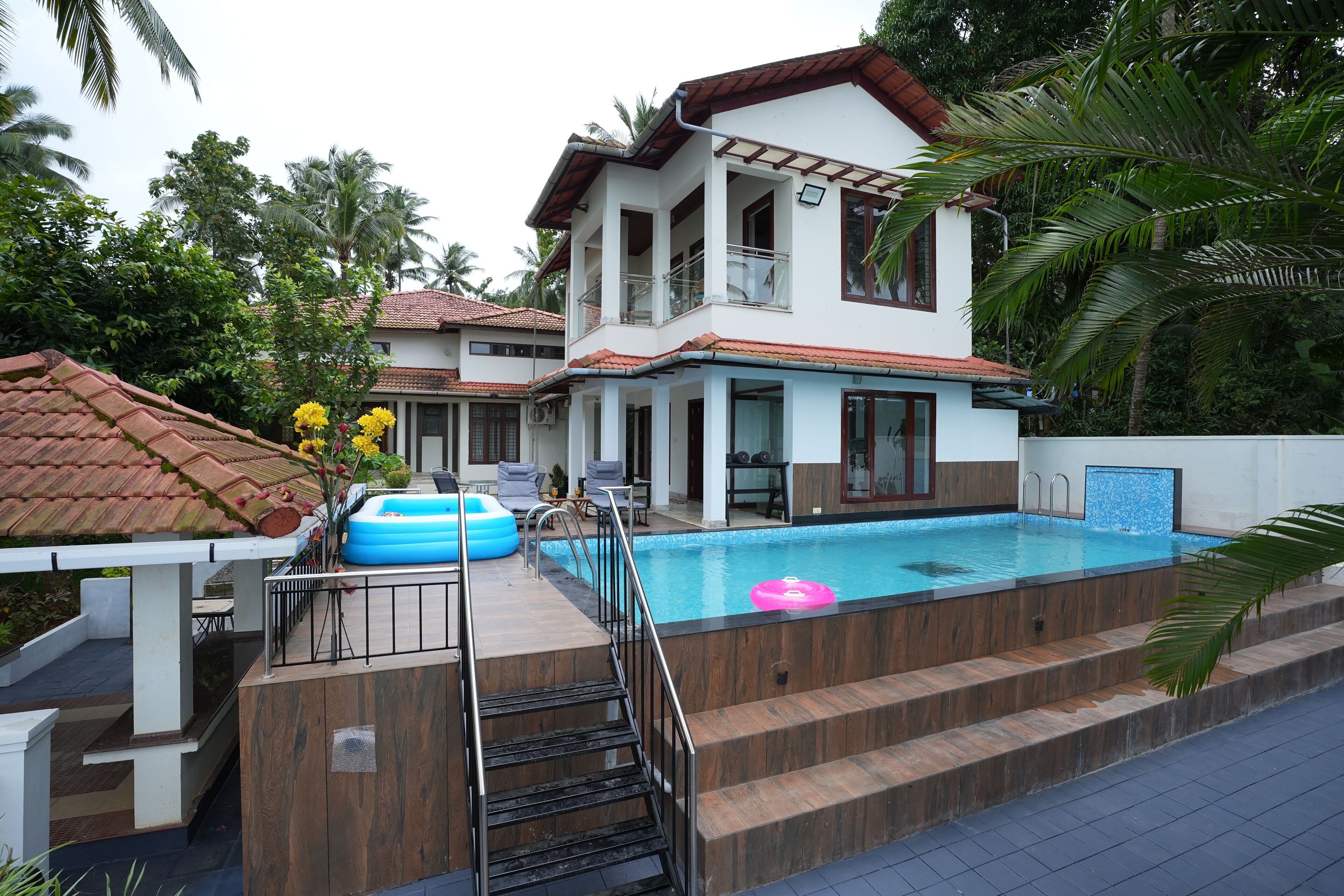 Una casa de dos pisos con piscina, mobiliario exterior y una escalera que conduce a la piscina.