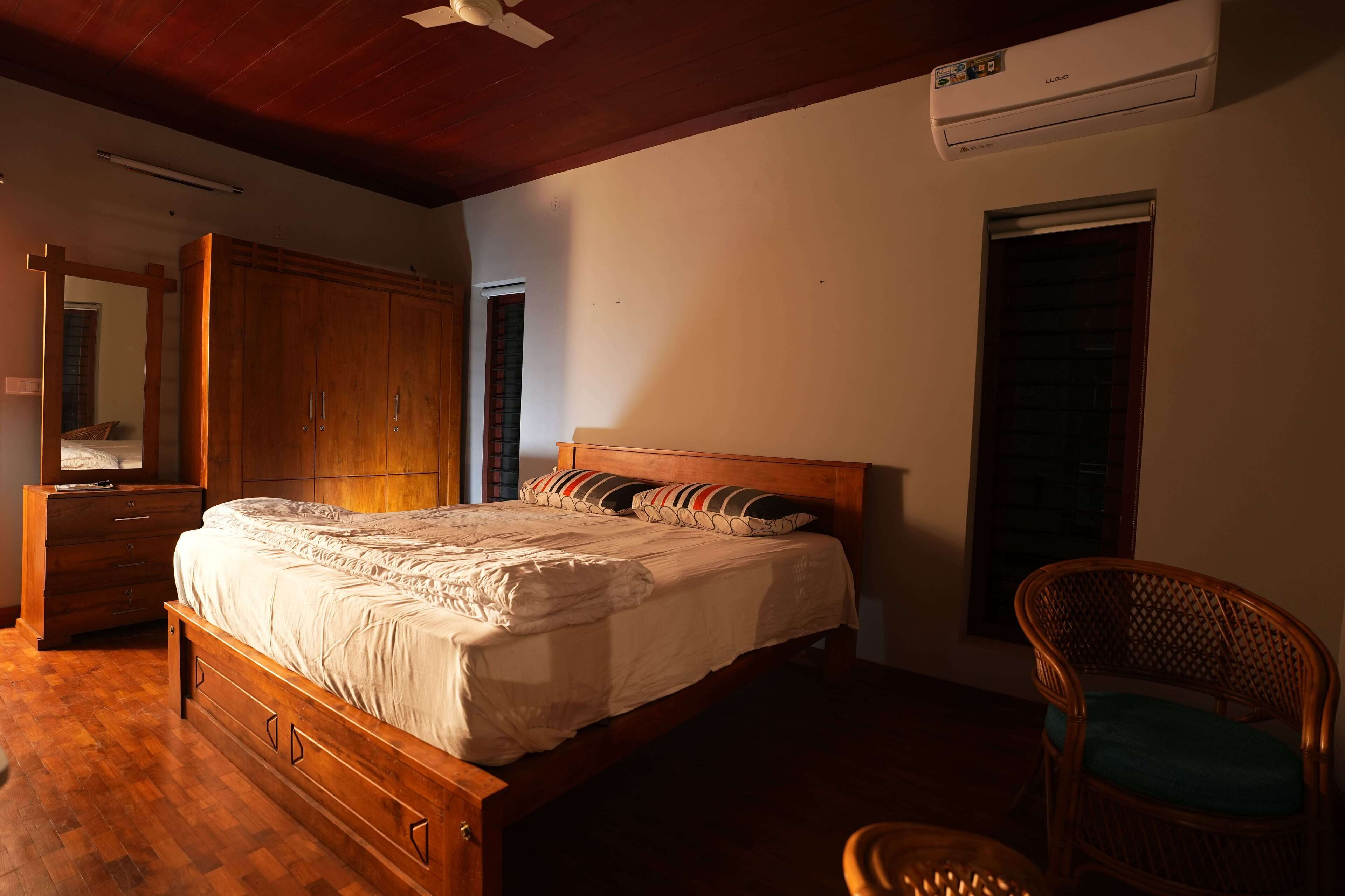 Un dormitorio con una cama de madera, un aparador, una silla y un equipo de aire acondicionado.