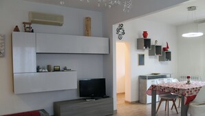 Un saló modern amb televisió de pantalla plana, prestatges integrats i zona de menjador amb taula i cadires.