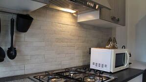 Cuina amb fogó de gas, microones i utensilis penjats.