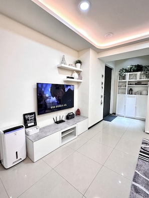A modern living room with a flat-screen TV, a white entertainment unit, a small white speaker, and a 'Welcome Guest' sign. - Tamsui Ocean Homestay Tamsui Dist. New Taipei. 2bedroom 2beds condo in welcome . (Tamsui)