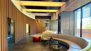 Een moderne lobby met gebogen zitplaatsen, een glazen scheidingswand en een wand van houten latten.