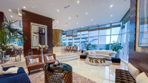 A spacious lobby with a large seating area, a grand staircase, and large windows offering a view of the outdoors.