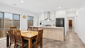 A modern kitchen with a central island, wooden dining table, and chairs. - Point Retreat in The Point (POINT LONSDALE)