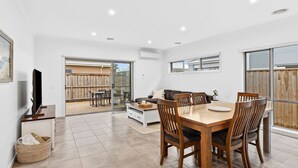 A spacious living area with a dining table, chairs, a sofa, and a TV. - Point Retreat in The Point (POINT LONSDALE)