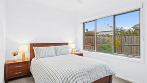 Une chambre à coucher avec un lit, deux tables de chevet, une fenêtre et une vue sur le jardin.