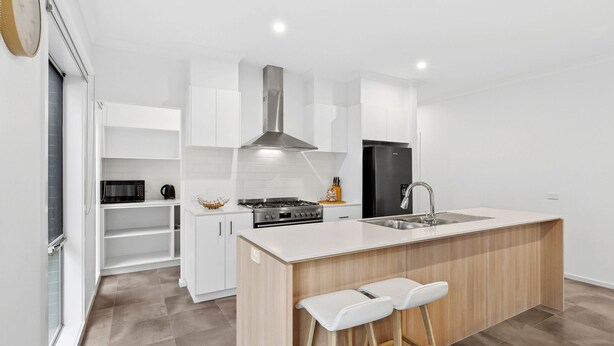 A modern kitchen with white cabinetry, a stainless steel range, a black refrigerator, and a wooden island with bar stools. - Point Retreat in The Point (POINT LONSDALE)