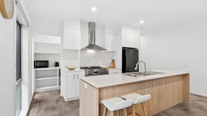 A modern kitchen with white cabinetry, a stainless steel range, a black refrigerator, and a wooden island with bar stools.