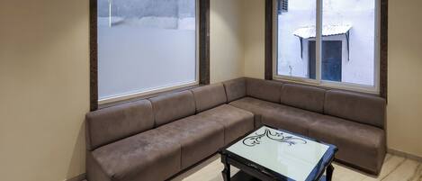 Ein Wohnzimmer mit einem braunen Ecksofa, einem Glastisch, großen Fenstern und einer Wanduhr.
