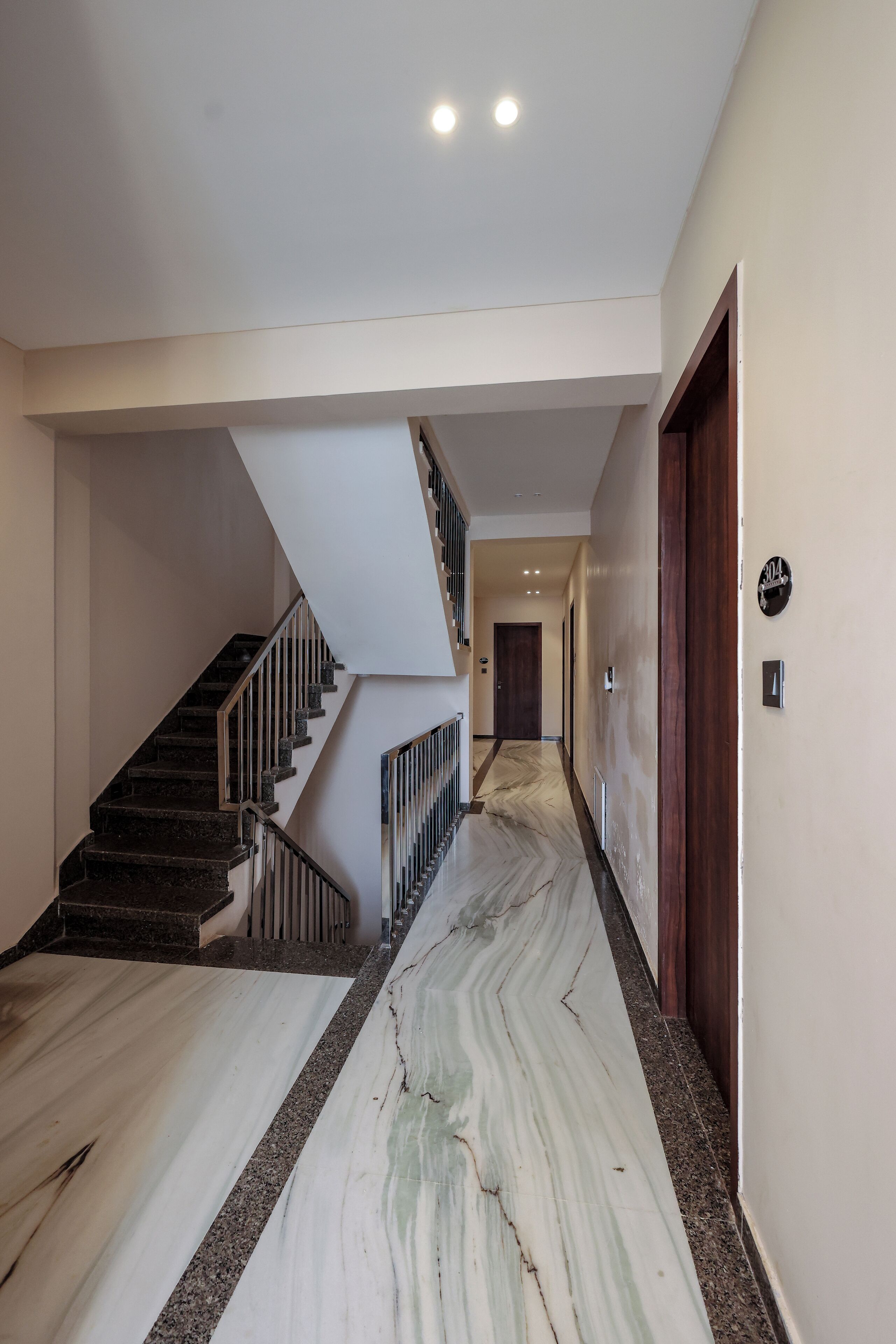 A modern interior with a marble floor, a staircase with metal railings, and a wooden door.