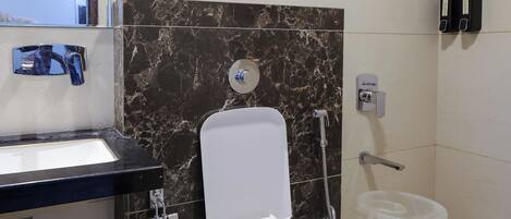 A modern bathroom with a white toilet, a sink with a black countertop, a marble wall, and a shower area.