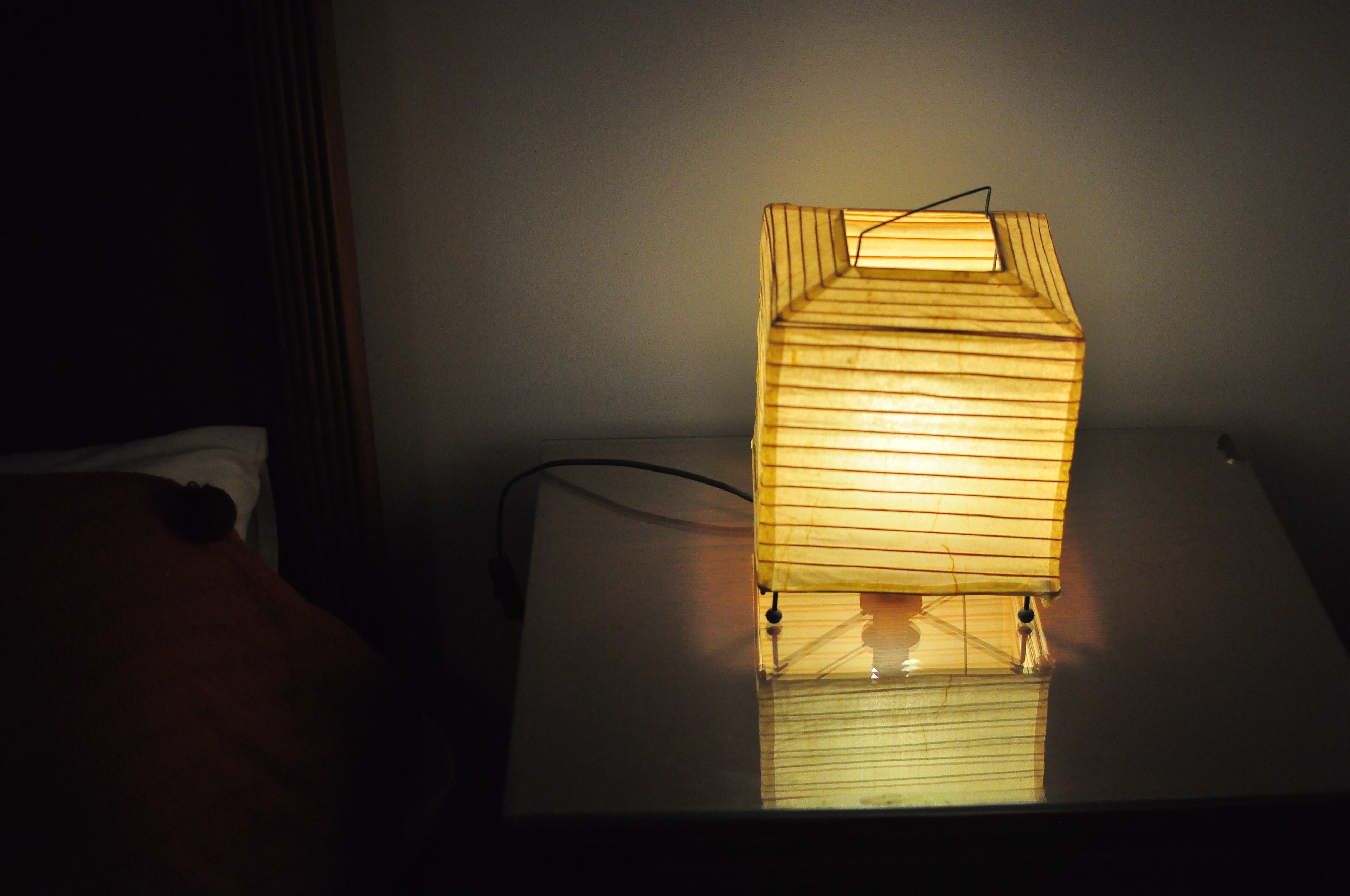 A bedside table with a wooden lamp casting light on the wall.