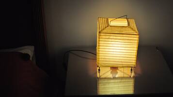 A bedside table with a wooden lamp casting light on the wall.