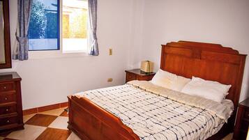 Un dormitorio con una cama de madera, una mesita de noche, un aparador y una ventana con cortinas.
