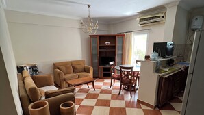 A living room with a checkered floor, a sofa, a dining table, and a kitchen area with a refrigerator and an air conditioner. - Morning Star Guesthouse (Sharm El Shikhe)