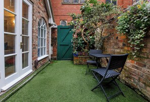 A small courtyard with artificial grass, a green gate, a brick wall, and a table with chairs.