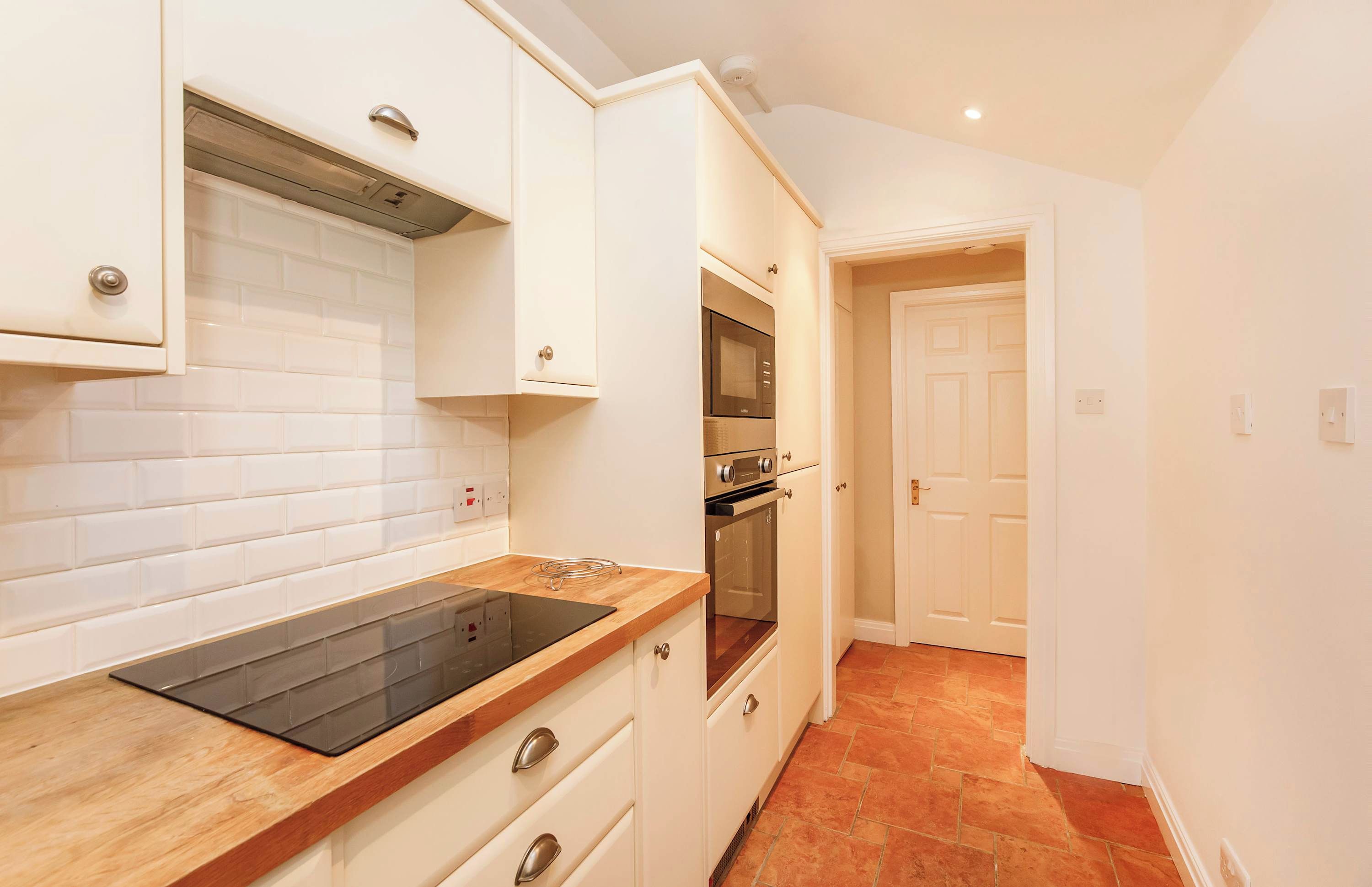 A kitchen with white cabinets, a black induction cooktop, and a built-in oven.